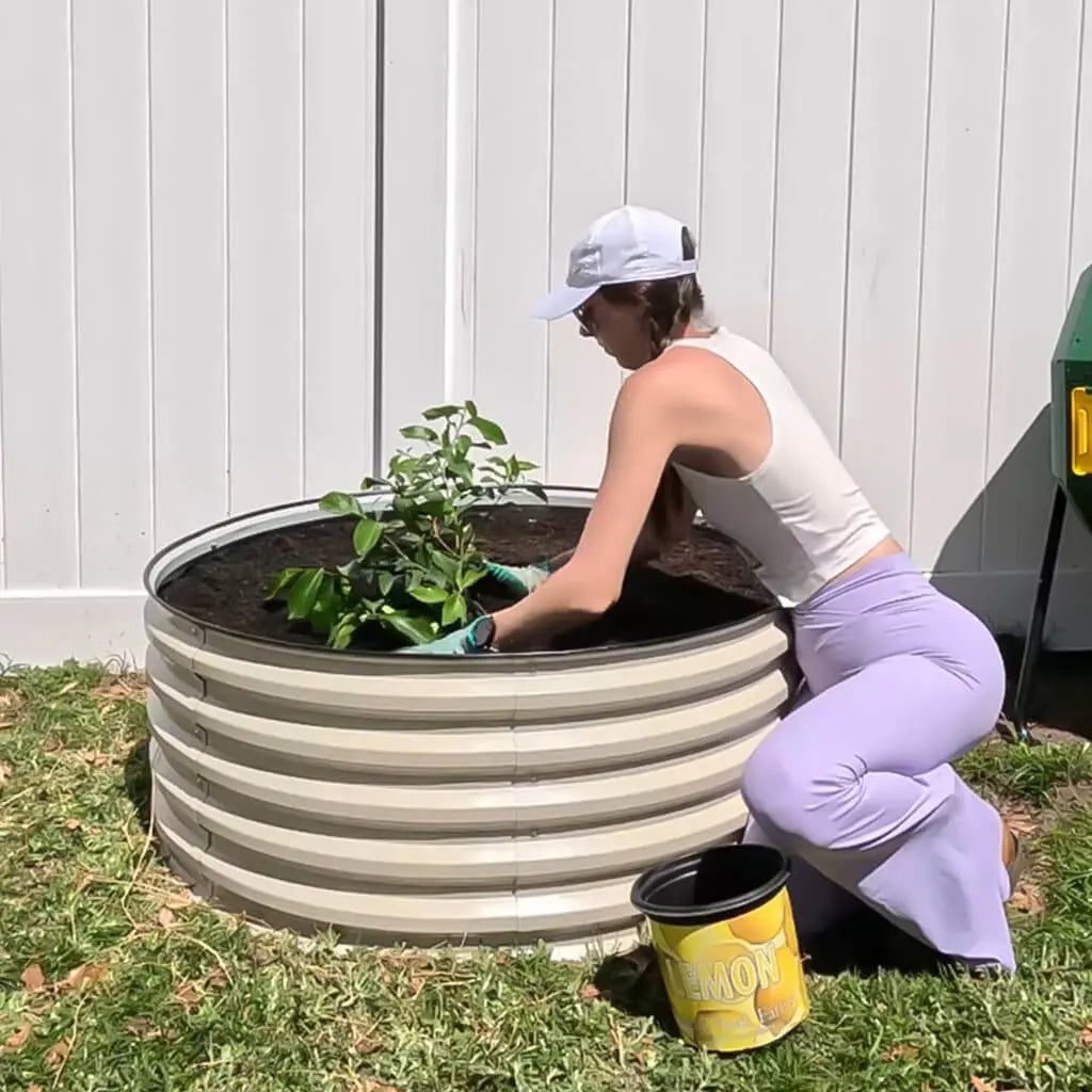 Cream round corrugated metal bed with a person planting a shrub.